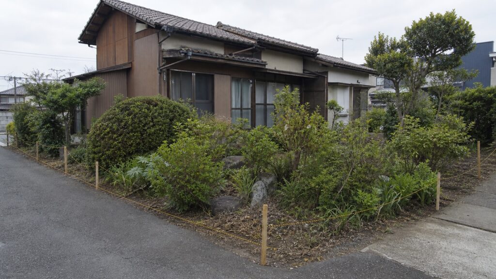 古い実家の庭と道路の間に境界確認用の杭と糸を配置した解体前計画のテーマ画像