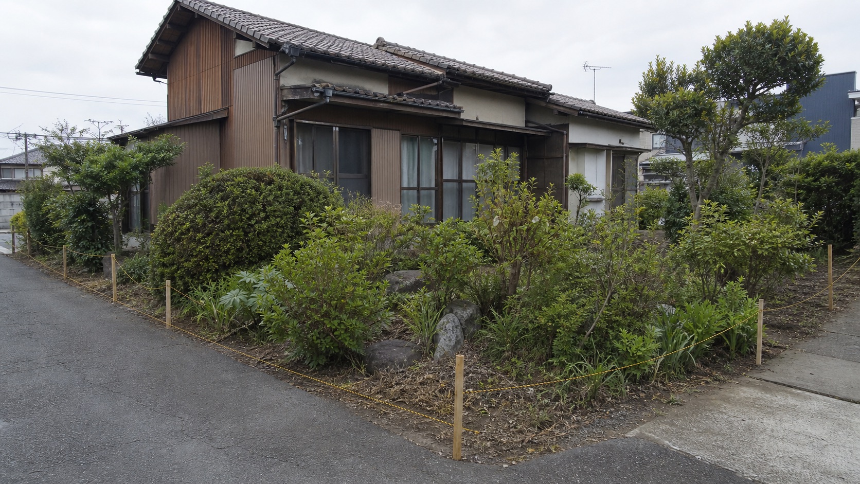 古い実家の庭と道路の間に境界確認用の杭と糸を配置した解体前計画のテーマ画像
